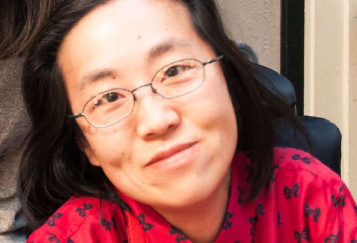 Asian American woman with long black hair and glasses. Her head is tilted slightly to the left side of the photo. She is wearing a red shirt with bows.