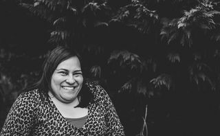 Black and white image of a woman seated with long dark hair. She is located on the lower left hand side of the photo and there is a large tree behind her.