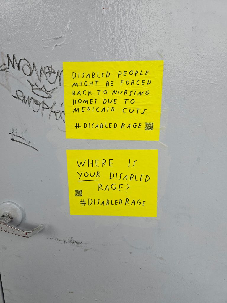 On a wall on a street are 2 signs on top of each other that are both in bright yellow with a QR code and #DisabledRage. The sign on top reads, “Disabled people might be forced back into nursing homes due to Medicaid cuts” and one below “WHERE IS YOUR DISABLED RAGE?”