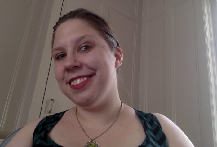 Young white woman smiling at the camera. Her hair is pulled back and she is wearing a tank top and a necklace.
