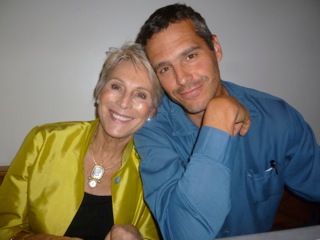 On older white woman leaning against her adult son. She is wearing a yellow silk jacket and he is wearing a blue shirt.