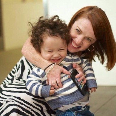 A woman with red hair who embracing her son with curly brown hair. He is giggling. She is smiling at the camera.