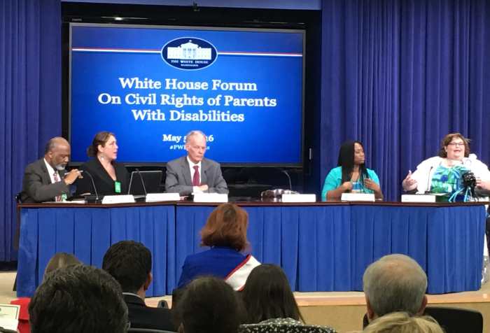 Five individuals sitting behind a draped table in front of a screen that reads "White House Forum on Civil Rights of Parents with Disabilities". At the end of the table is a brunette haired woman sitting in a wheelchair and speaking passionately. Photo courtesy of Rebecca Cokley.