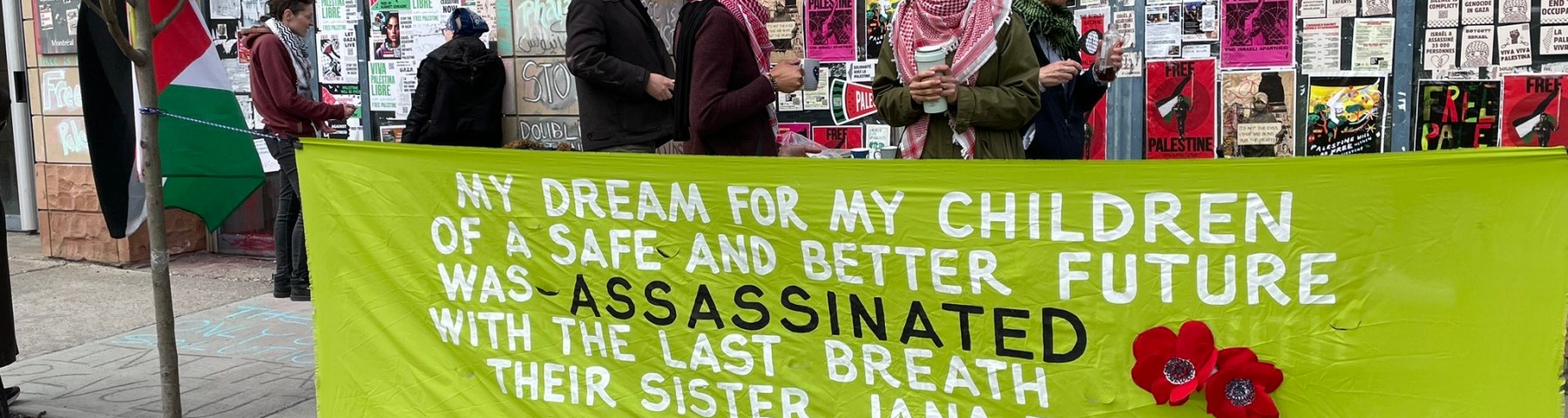 Photo of Samar AlKhdour wearing a light pink baseball cap and a red and white Keffiyeh standing in conversation with a sit-in supporter in front of Canadian Minister of Immigration Marc Miller’s riding office in Montreal on April 29, 2024. Behind them are the Immigration minister’s outside office-building walls covered in posters and stickers in support of Palestinian liberation. In the foreground, there is a bright green banner with the words: “My dream for my children of a safe and better future was assassinated with the last breath their sister Jana took on 8/1/24 in Gaza.” The lettering is white and black. There are also red Palestinian poppy flowers sewn into the banner. Photo by Nelly Bassily