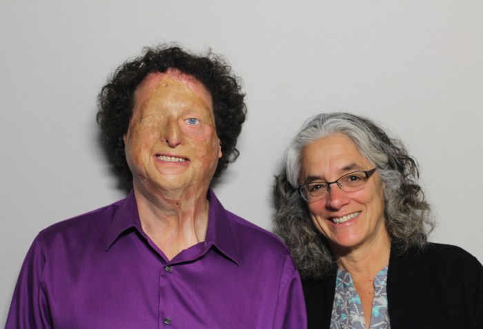 Image Description: A photo featuring Joshua Miele and Lainey Feingold taken on August 21, 2014. The man on the left is Joshua Miele. He appears to be white, and is wearing a purple button-up shirt. He has curly brown hair, one blue eye and scars on his face. He is looking at the camera and smiling. The woman on the right is Lainey Feingold. She appears to be white, has medium-length salt and pepper hair, and is wearing glasses with a black cardigan and a blue shirt. She is looking at the camera and smiling.
