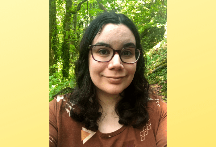 Graphic with a pale yellow gradient featuring a headshot of a woman with light brown skin and shoulder-length black, wavy hair wearing purple glasses and a brown and orange patterned shirt. She’s smiling. There’s a forest in the background.