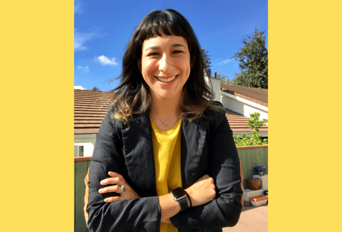 Graphic with a yellow background. A medium-skinned person with black hair worn long around their shoulders and short baby bangs, smiling outdoors, with a blue sky in the background.