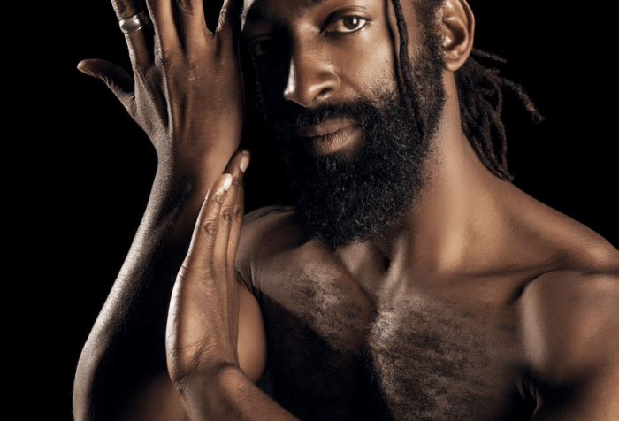image of Antoine Hunter, a self-described handsome, dark milk chocolate, African American Man. He has long Ebony dreadlocks hair tied to back leaving one deadlock on the side of his face which is close to his eyes. He has a full 1-inch long Ebony-colored bread and full brown lips. He is bare chested and his right hand is to the side of his face with his left hand touching his right forearm. His eyes look straight at you with honest spirit.