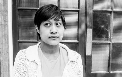 Black-and-white photo of an Indonesian woman in a cardigan and dress, with a door as backdrop. Picture credit: Wasi Daniju.