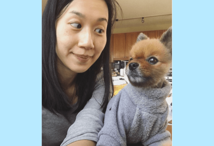 Graphic with a light blue background featuring a Taiwanese woman with black shoulder length hair and a grey shirt, side-eyeing a teddy-bear looking Pomeranian who dresses in a grey turtleneck sweater.